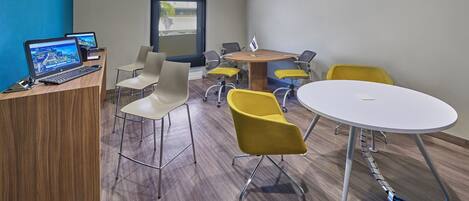 Una sala de conferencias moderna con un mostrador de recepción de madera, múltiples sillas, una mesa redonda y un ventanal grande.