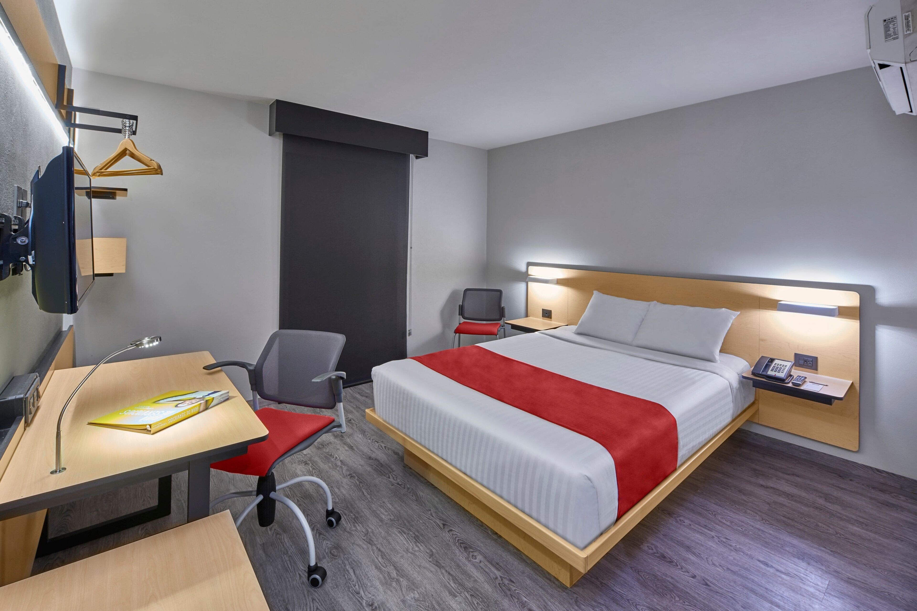 A hotel room with a bed, desk, chair, and bedside table.