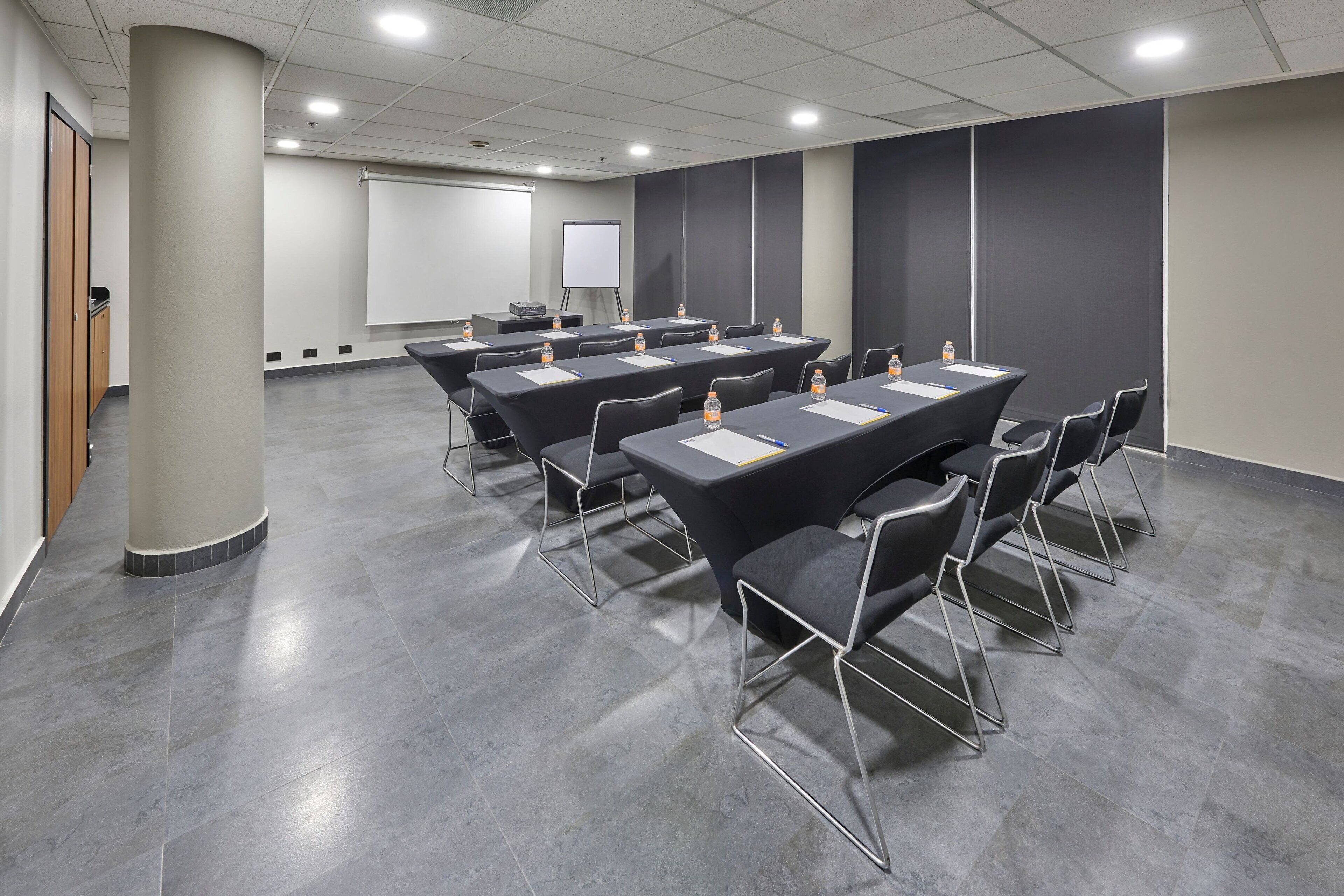 A conference room with a large table, chairs, a projector screen, and a whiteboard.