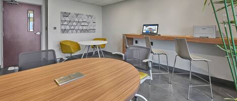 A conference room with a wooden table, yellow chairs, a white round table, and a Samsung printer on a shelf.