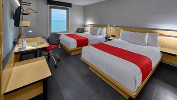Habitación de hotel con dos camas, un escritorio, una silla, un televisor y ventana con vista al mar.