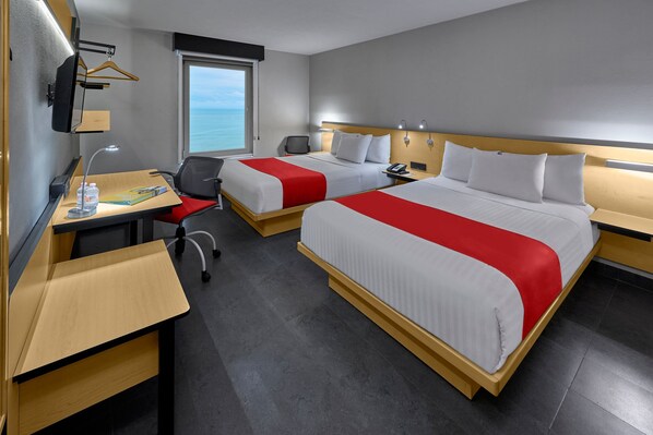 A hotel room with two beds, a desk, a chair, a TV, and a window with a view of the sea. - City Express by Marriott Veracruz (Boca del Río)
