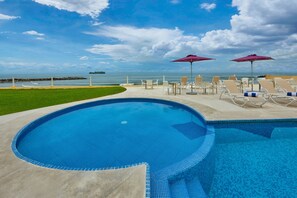 A swimming pool with lounge chairs and umbrellas, a grassy area, and a view of the ocean. - City Express by Marriott Veracruz (Boca del Río)