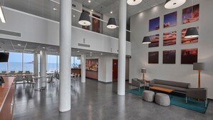 Un hall espacioso con techos altos, ventanas grandes y una zona de estar con sofá y otomanas.