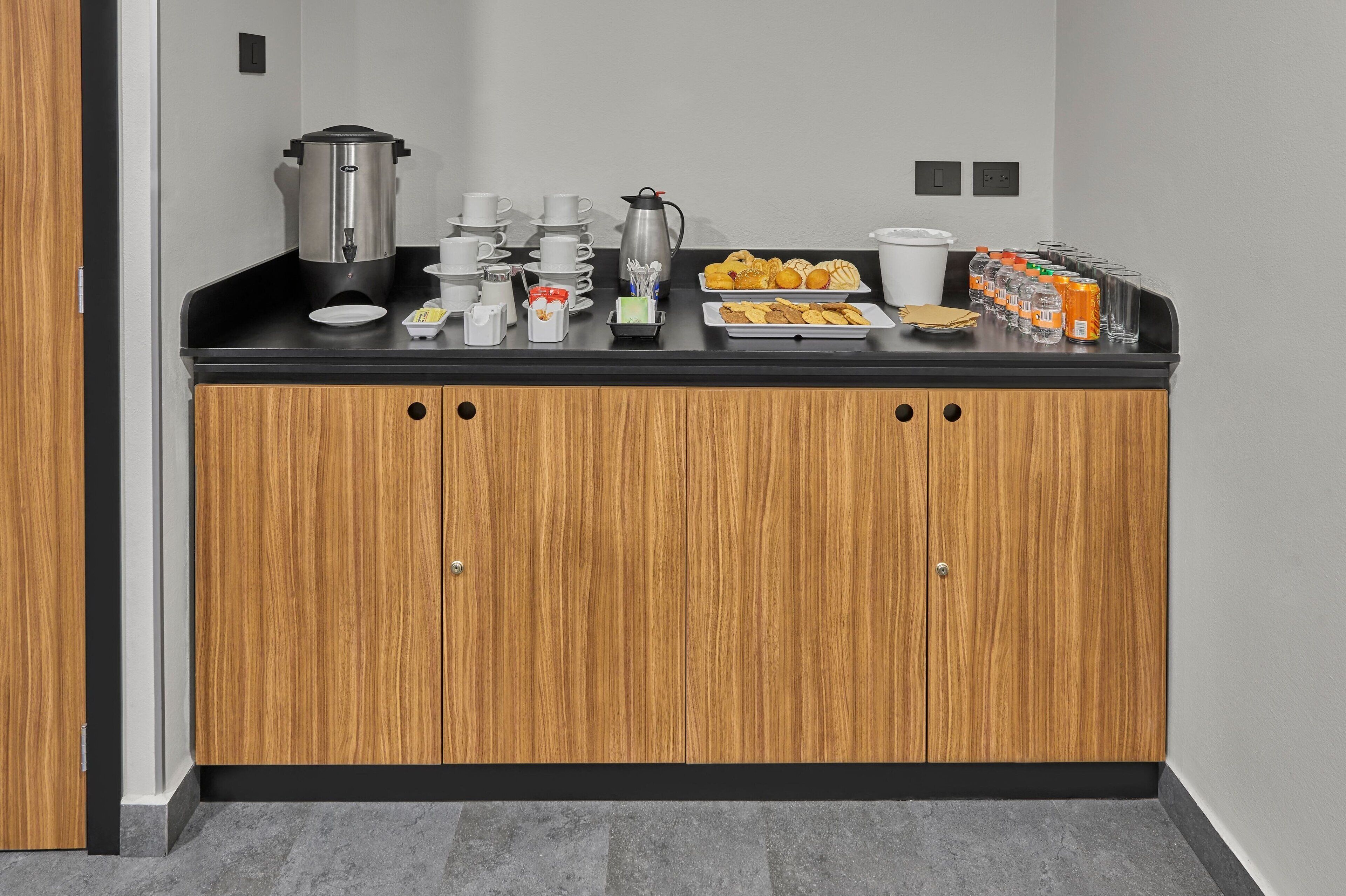 A breakfast bar with coffee makers, cups, and pastries.