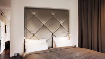 A modern hotel room with a large bed, a tufted headboard, and a dark curtain.
