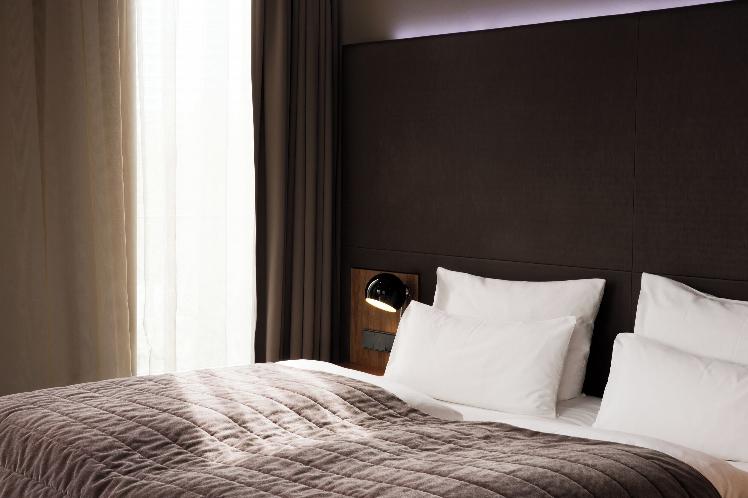 A neatly made bed with a quilted cover, a headboard with a built-in nightstand, and a bedside lamp.