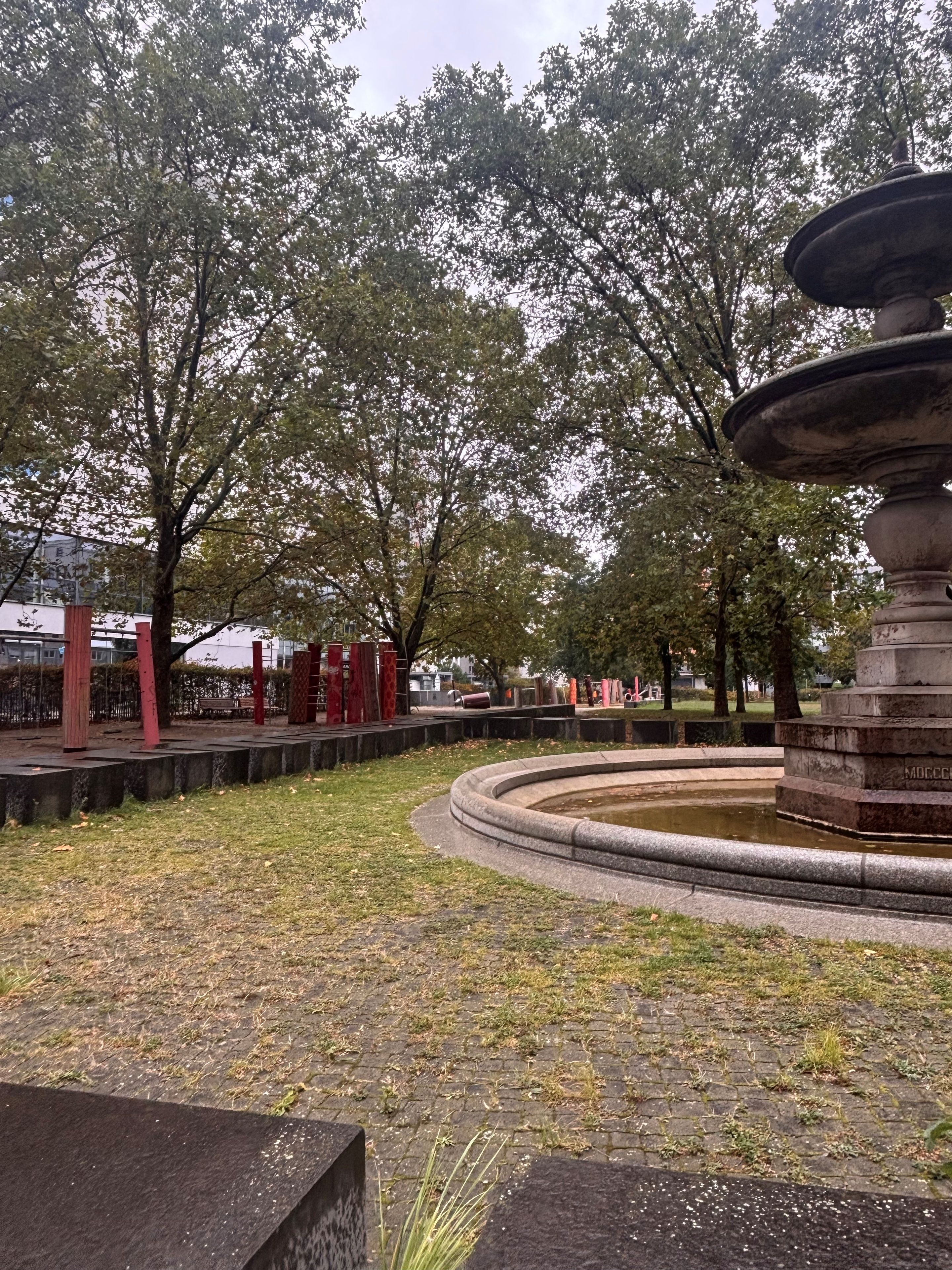 Ein Park mit einem Brunnen, Bäumen und einem gepflasterten Weg.