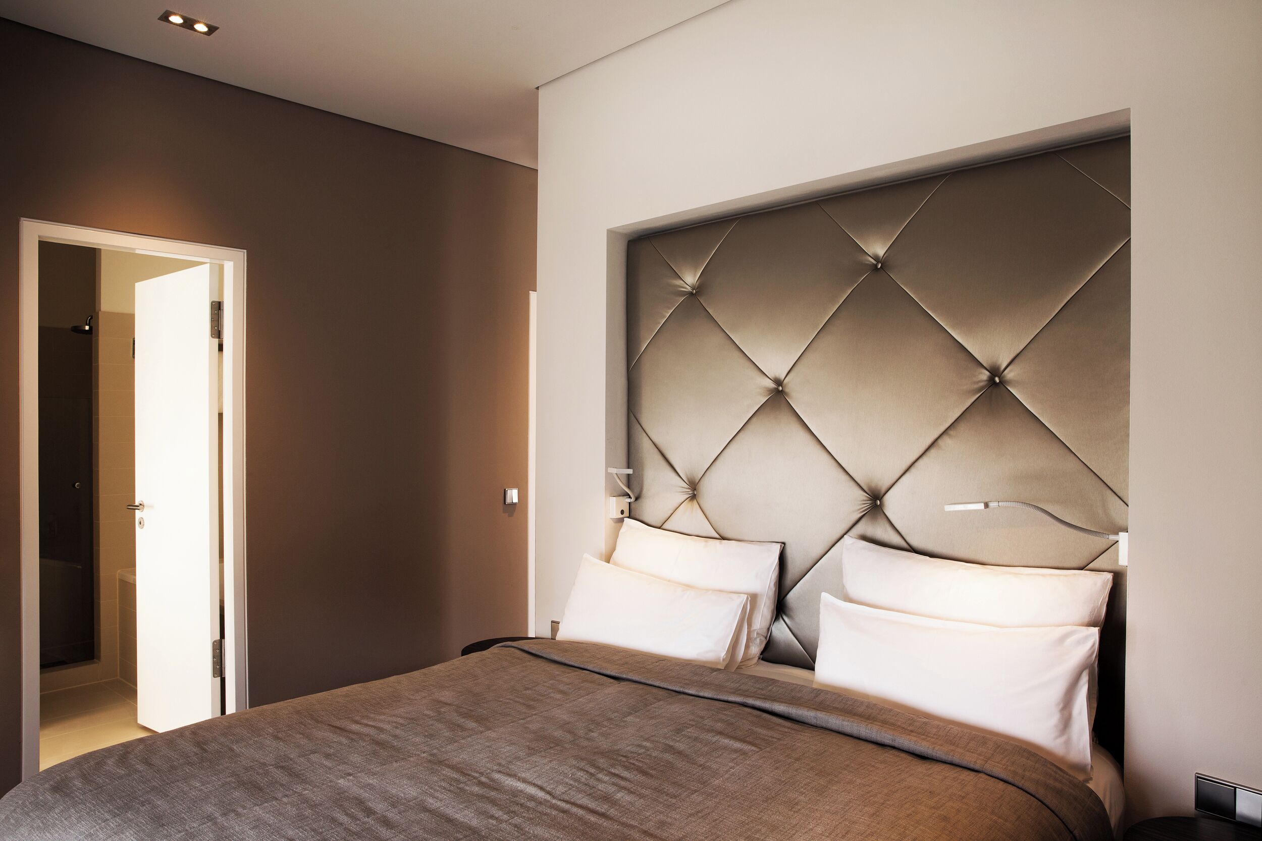 Un dormitorio moderno con cabecera capitonada, una paleta de colores neutros y una cama grande con muchas almohadas.
