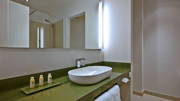 A bathroom with a white sink, green countertop, and a large mirror. There are three bottles on the counter.