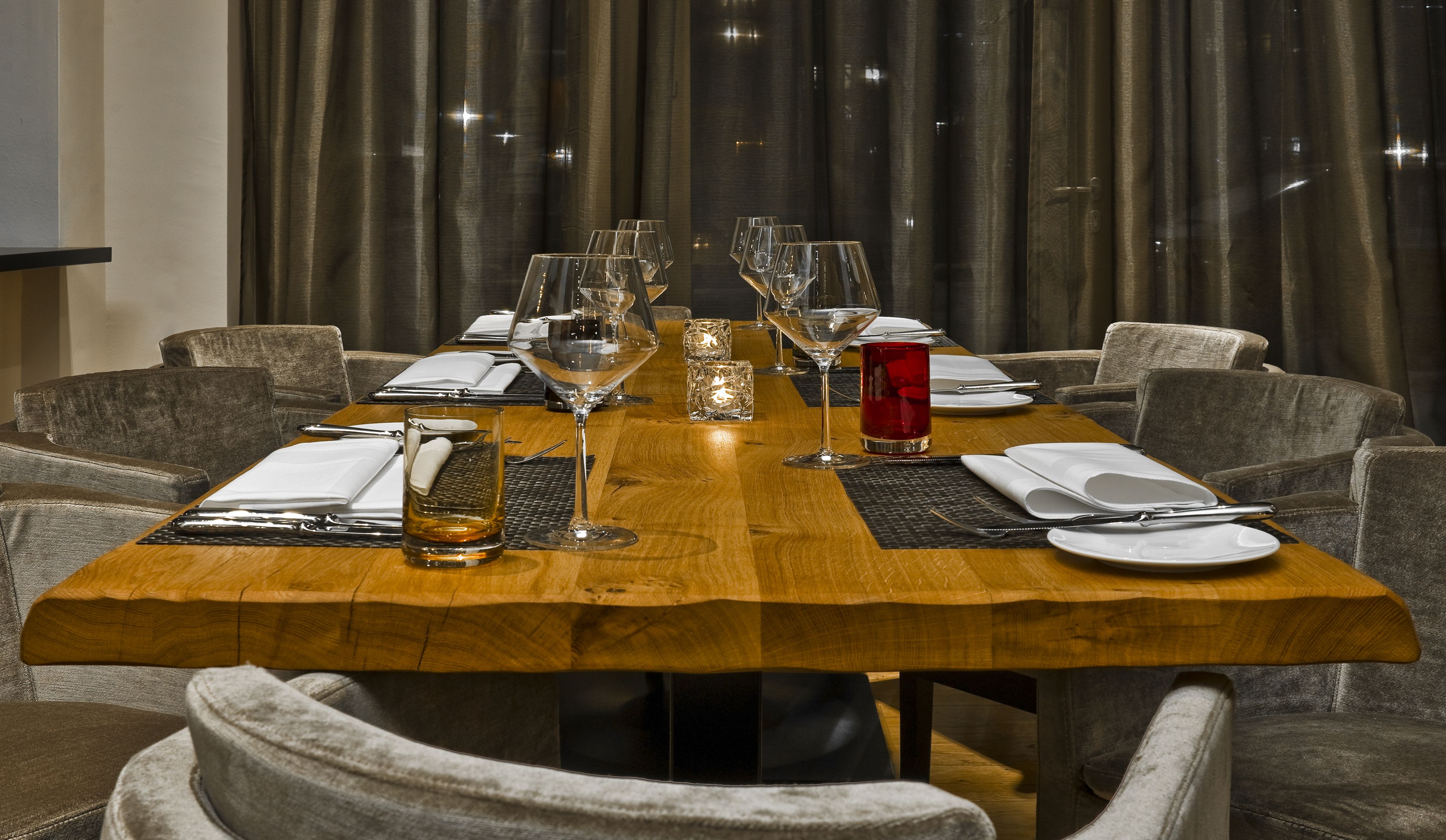 Una mesa de comedor dispuesta con varias copas de vino, una bebida roja y cubiertos.