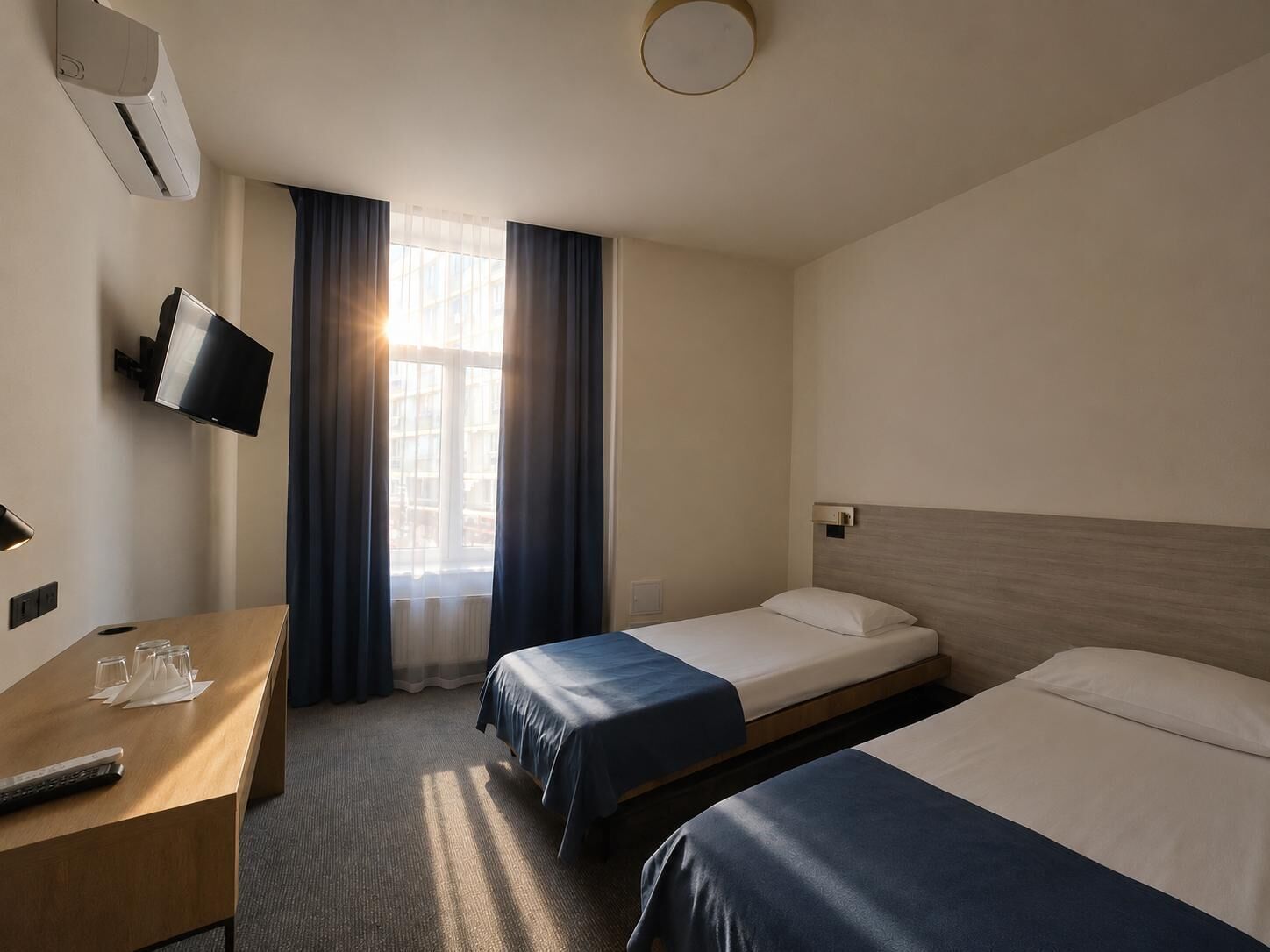 A hotel room with two beds, a desk with a TV, and a window with curtains.