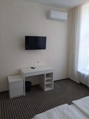 Hotelkamer met een bed, een bureau met een televisie, een kastje en een airconditioning aan de muur.