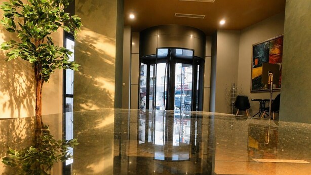 Un vestíbulo con puerta de cristal, una planta y un cuadro en la pared.