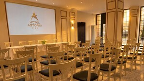 Un salón de conferencias con múltiples sillas blancas y una pantalla de proyector que muestra 'HOTEL ASTORIA'.