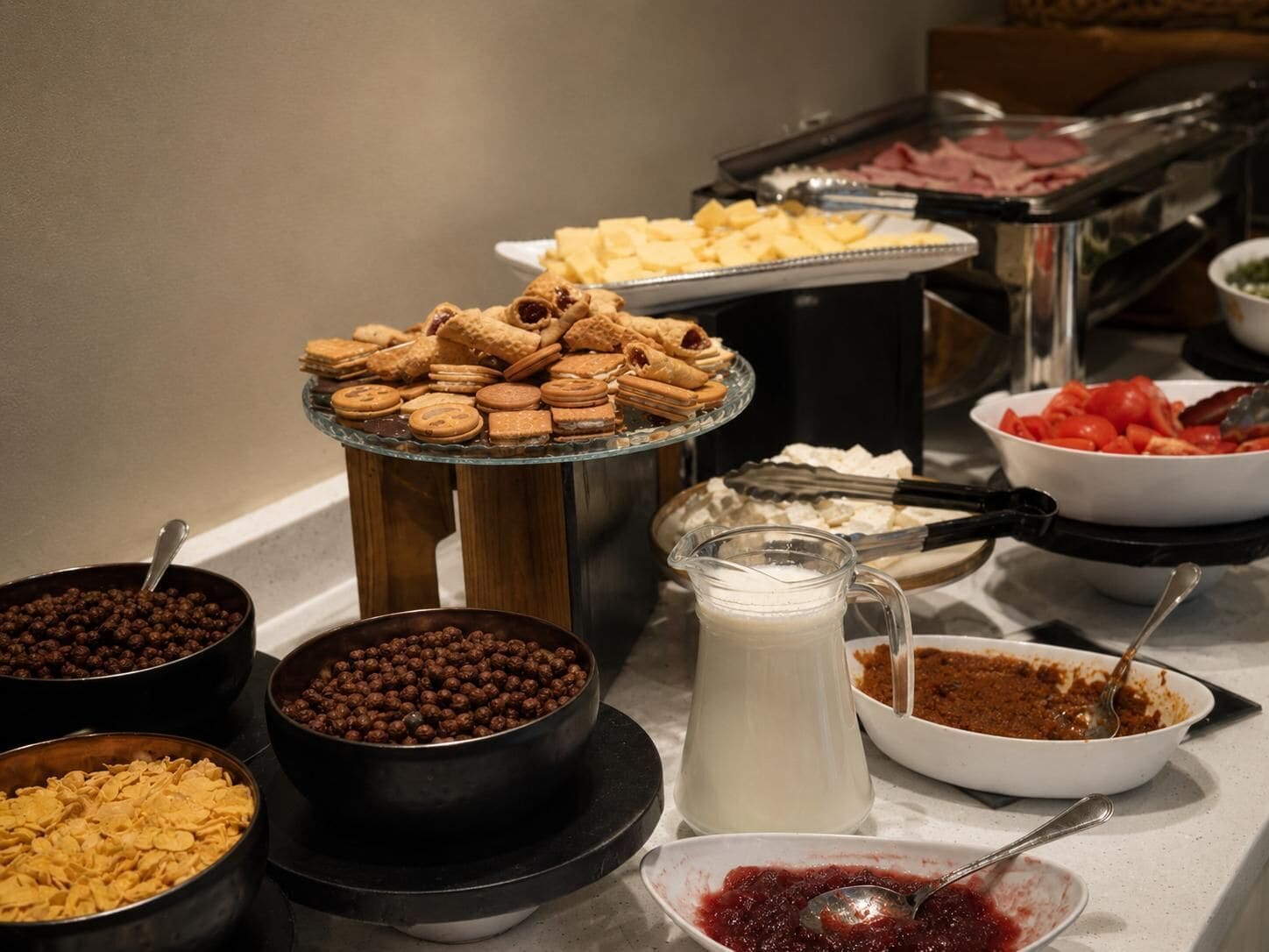 A buffet with various food items including cookies, cereal, milk, and a bowl of red fruit.