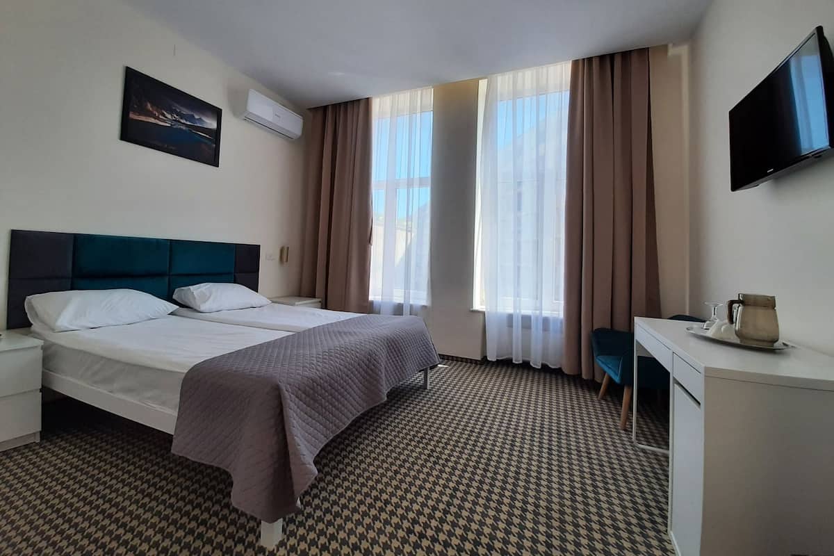 Una habitación de hotel con cama, escritorio, televisor y ventana con cortinas.