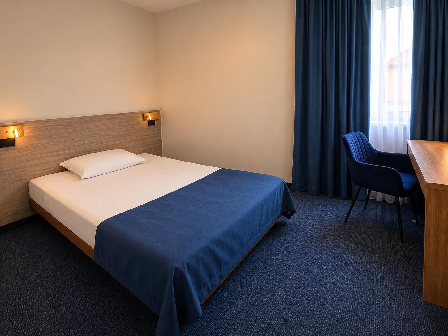 Una habitación de hotel con cama, escritorio, silla y ventana con cortinas.