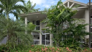 A multi-story building with a covered outdoor area, surrounded by lush greenery and flowering plants.