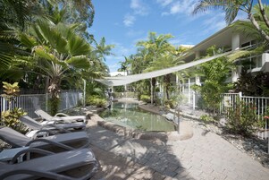 Un área de piscina con sillas de descanso, un pequeño elemento acuático y plantas tropicales a su alrededor.