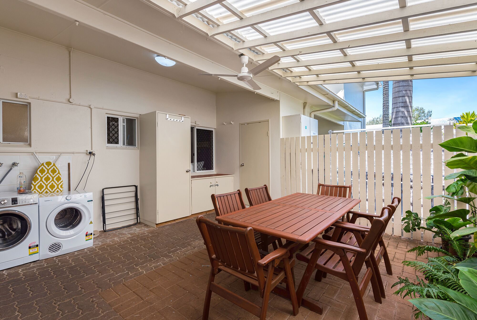 Une terrasse avec une table et des chaises en bois, un lave-linge et un ventilateur de plafond.