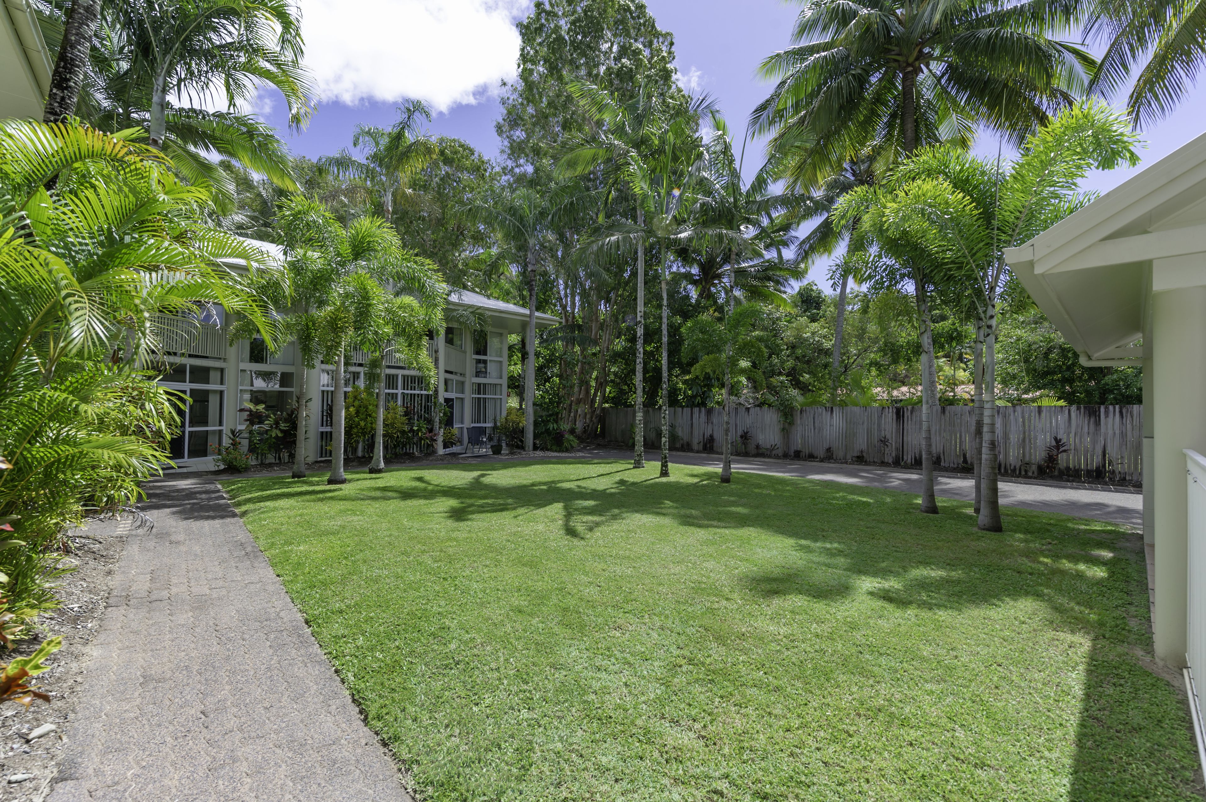 A well-maintained yard with a paved walkway, palm trees, and a wooden fence.