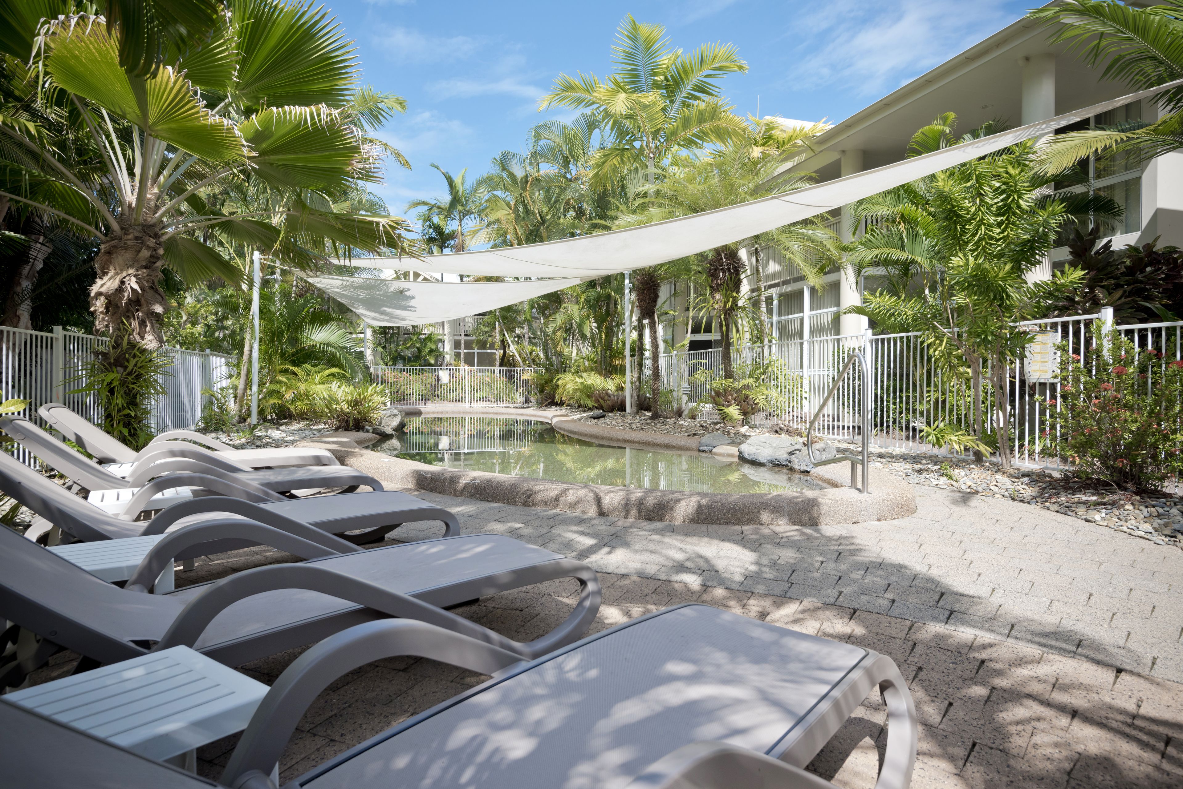 Un área junto a la piscina con sillones de descanso, un pequeño estanque y plantas tropicales.