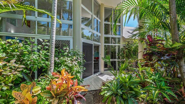 A modern building with large glass windows and a lush garden with various tropical plants.