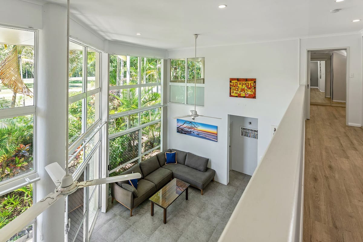 Un amplio salón con ventanas grandes, un ventilador de techo y un sofá moderno.