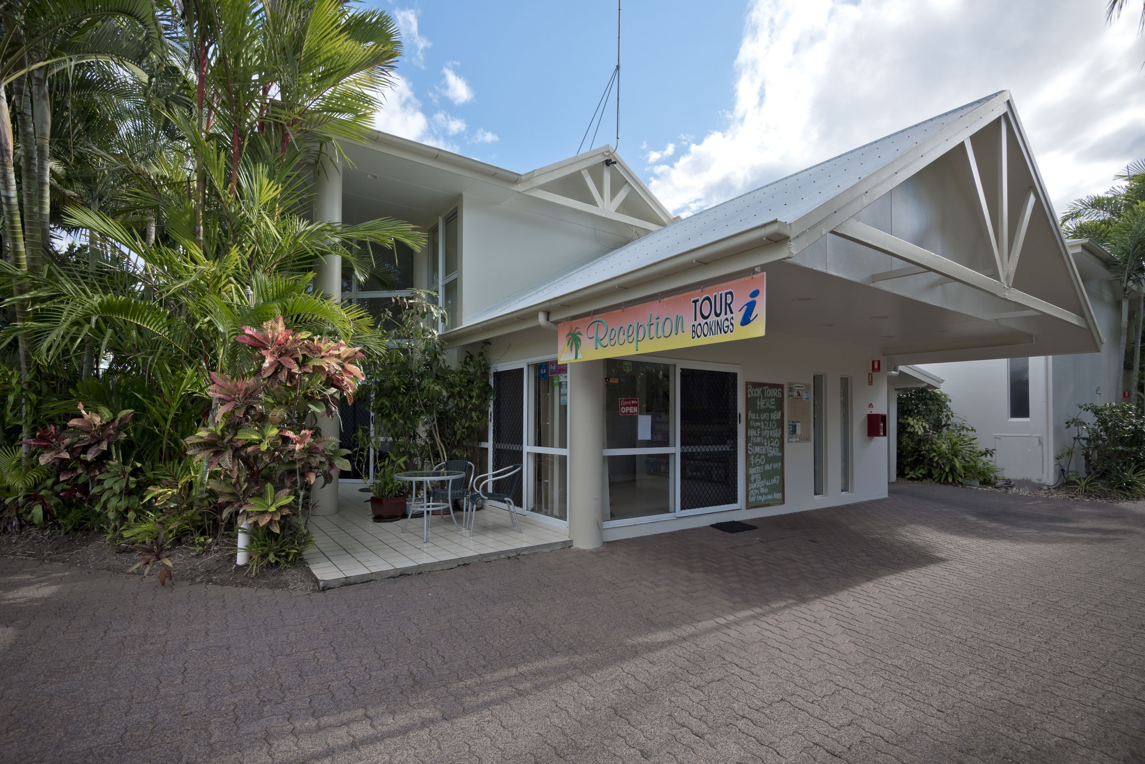 A reception area with a sign for tour bookings, a covered outdoor seating area, and a building with a white facade.