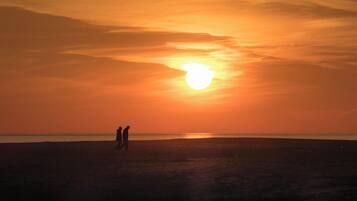 Un coucher de soleil sur une plage, avec deux personnes dont les silhouettes se détachent sur le ciel.