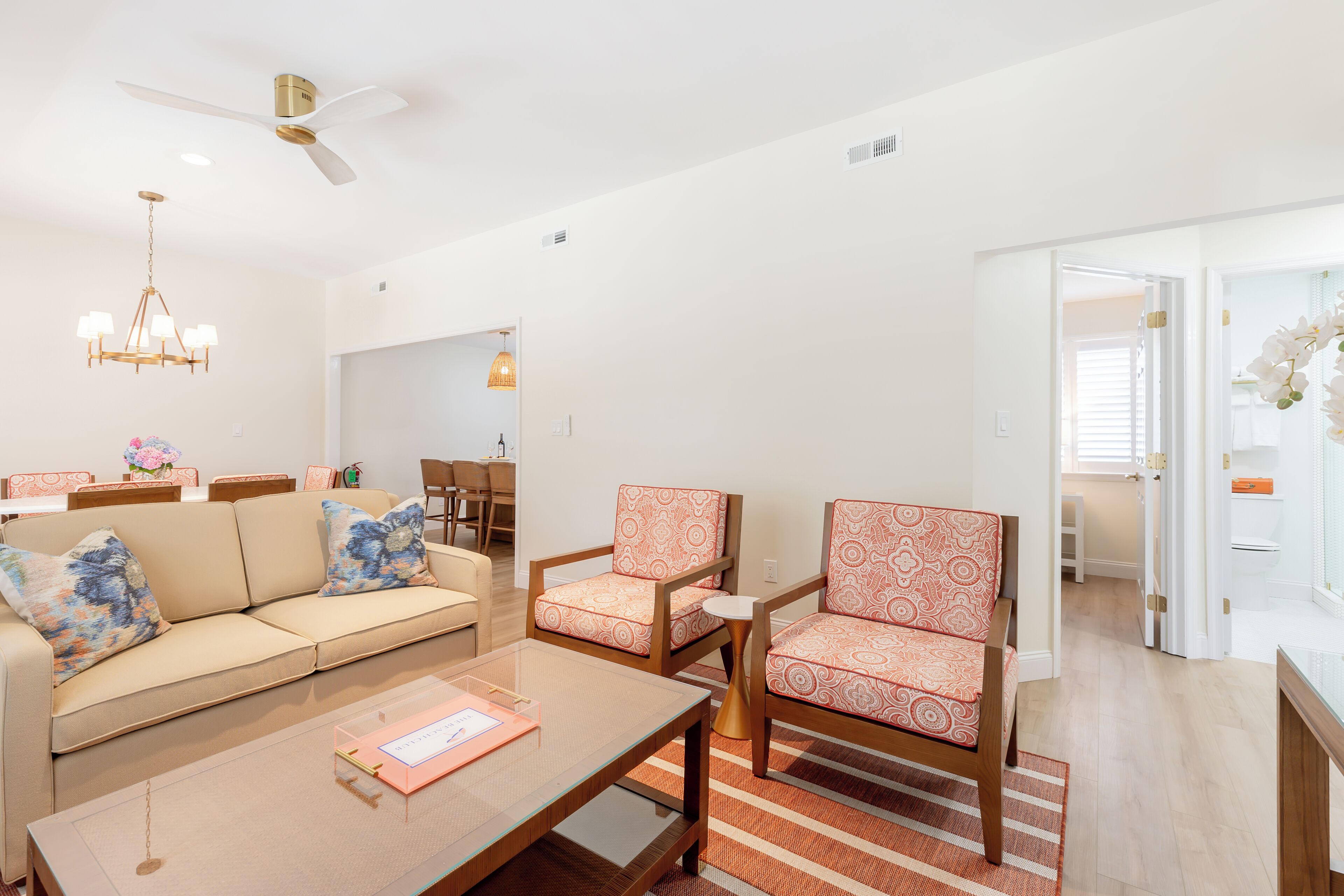 Una sala de estar moderna con un sofá, sillones, una mesa de centro y un ventilador de techo.