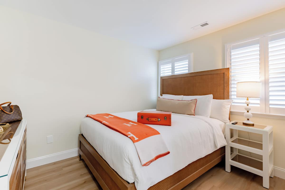 A neatly made bed with a wooden headboard, a bedside table with a lamp, and a suitcase on the bed.