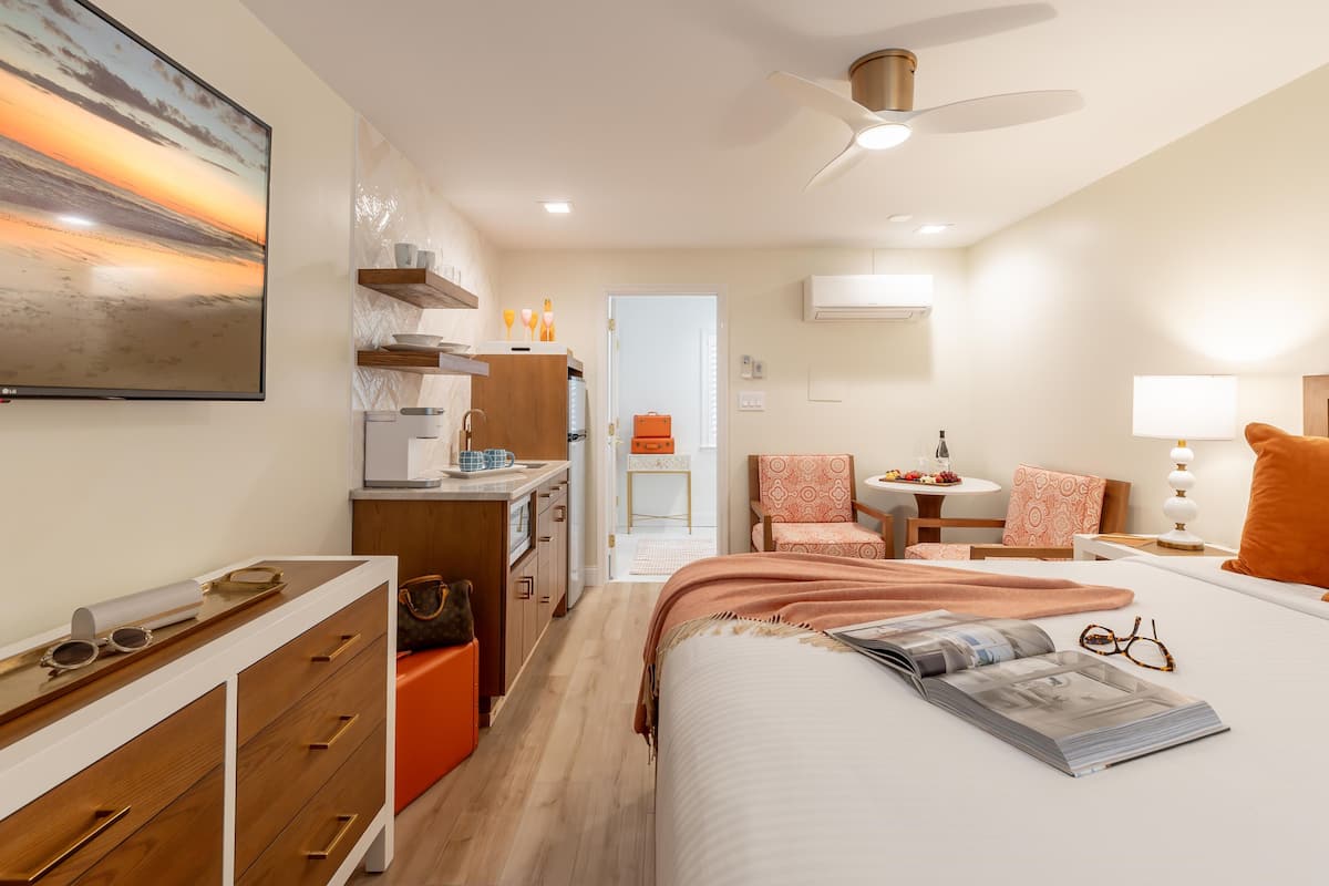 A modern hotel room with a bed, a desk, a chair, a TV, and a ceiling fan.