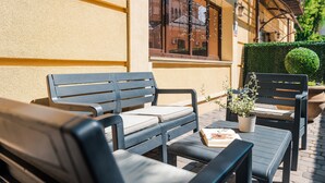 Un área de estar al aire libre con una mesa, dos sillas, una planta en maceta y un ventanal con vistas a edificios.