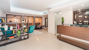 Un moderno vestíbulo de hotel con mostrador de recepción, zona de estar y una estantería con diversos objetos.