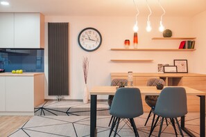 Una cocina moderna con horno empotrado, un comedor con mesa y sillas de madera, y un reloj montado en la pared.