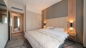 Una habitación de hotel moderna con una cama grande, un armario empotrado, una mesita de noche con lámpara y un espejo.