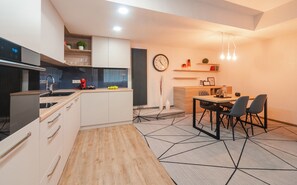 Una cocina moderna con armarios blancos, una estufa negra y una encimera de madera. Hay un comedor con una mesa y sillas, y un reloj en la pared.