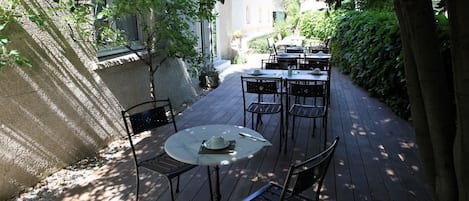An outdoor patio with tables and chairs, surrounded by greenery and a stone wall.