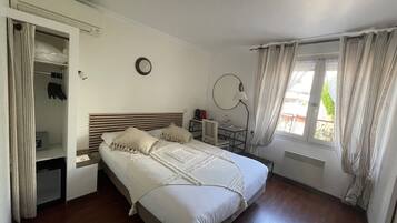 Une chambre à coucher comprenant un lit, un bureau, une chaise, une armoire et une fenêtre avec des rideaux.