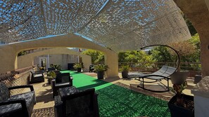 Un patio al aire libre con muebles de mimbre, plantas en macetas y un césped verde.