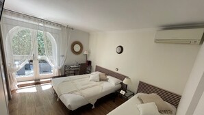 Una habitación de hotel con dos camas, un escritorio, una silla, un ventanal con cortinas y un equipo de aire acondicionado.