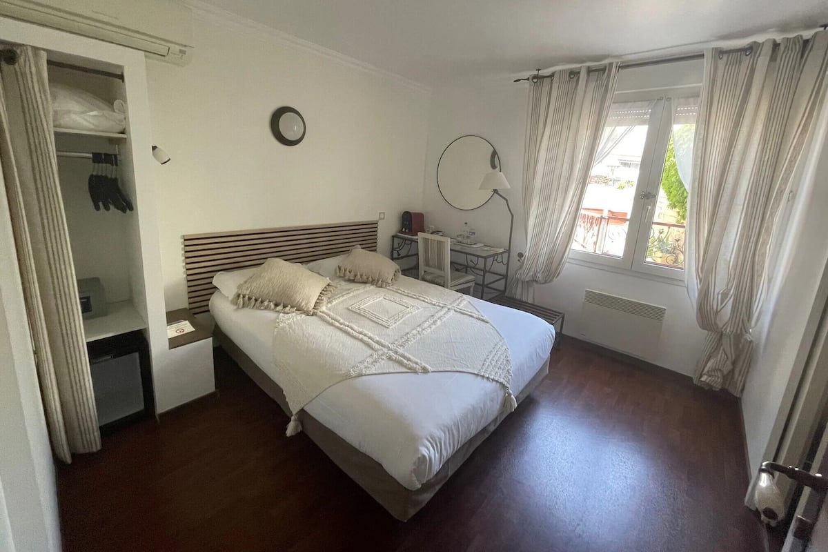 Une chambre à coucher comprenant un lit, un bureau, une chaise, une armoire et une fenêtre avec des rideaux.