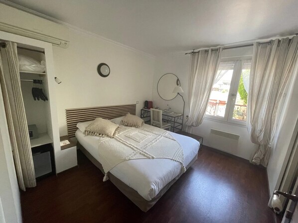 Un dormitorio con cama, escritorio, silla, armario y ventana con cortinas.