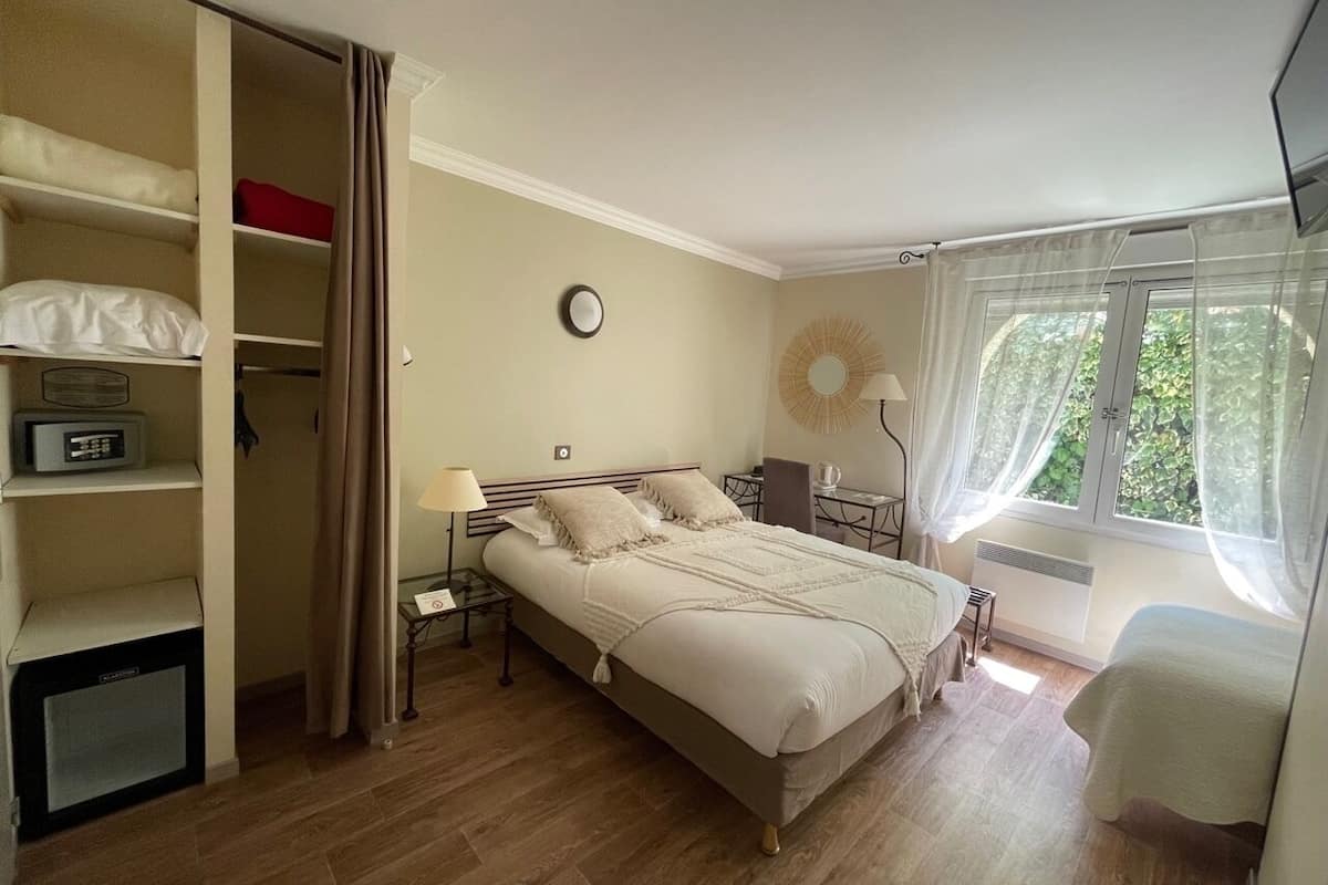 Une chambre à coucher comprenant un lit, des tables de chevet, une armoire, un radiateur et une fenêtre avec des rideaux.