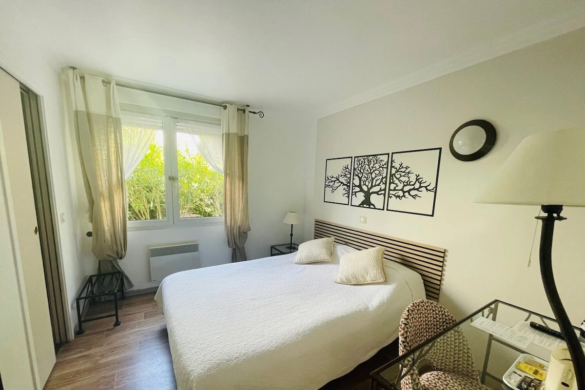 Une chambre avec un grand lit, une chaise, un bureau et une fenêtre avec des rideaux.