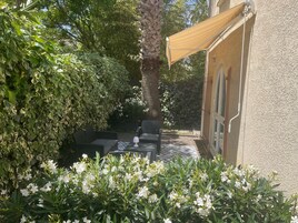 Un patio al aire libre con una mesa y sillas, rodeado de abundante vegetación y flores blancas.