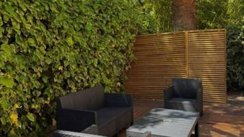 Una terraza con mobiliario exterior, una valla de madera y un seto.
