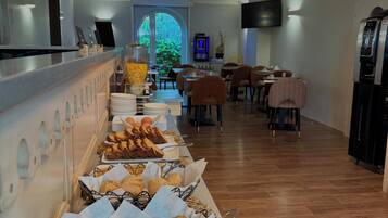 A buffet with various baked goods, a seating area with tables and chairs, and a large window with a view of greenery.